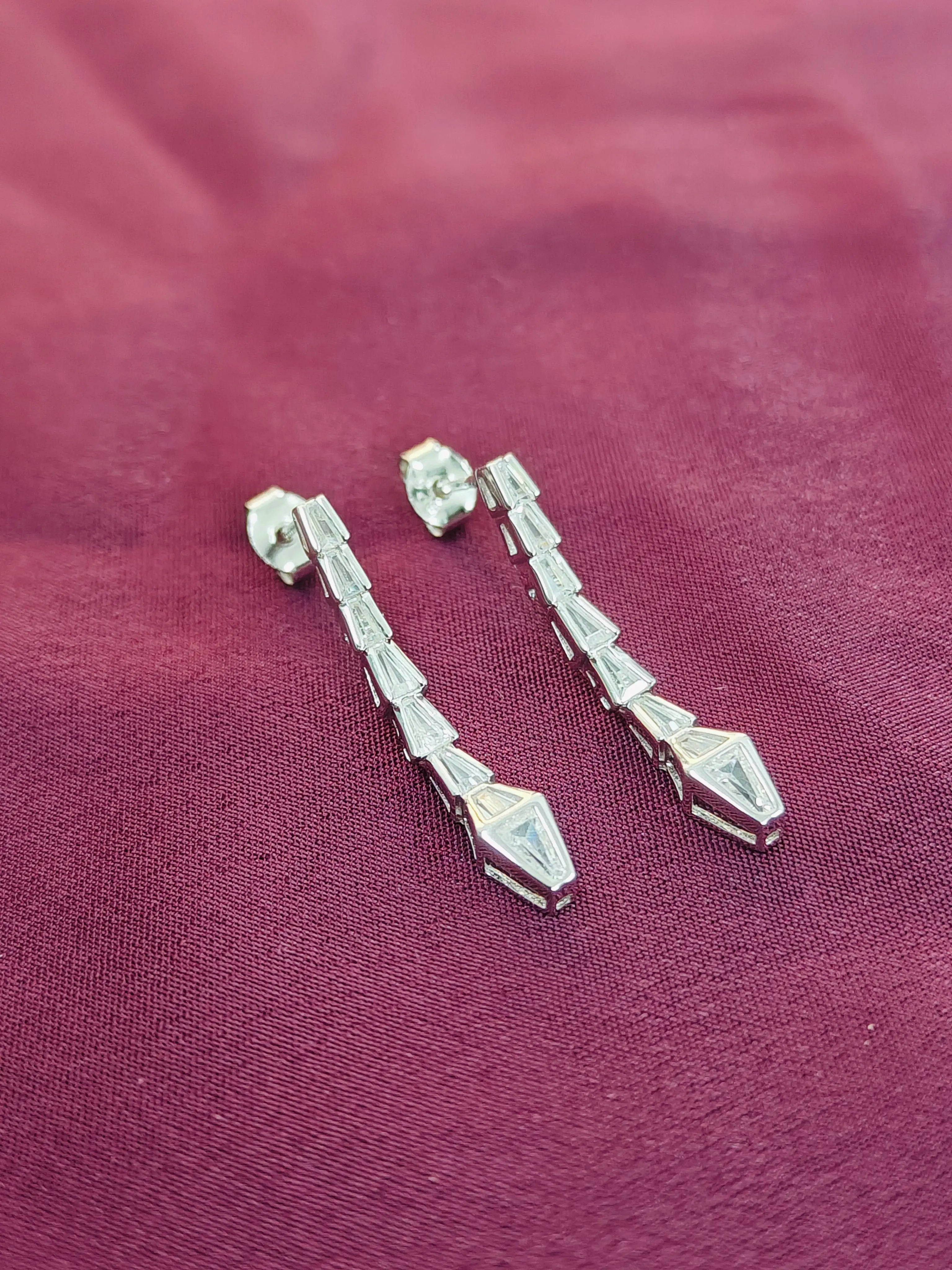 Silver earrings on a maroon fabric background